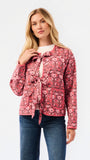 A woman modeling a pink floral patterned jacket with a tie-front detail and front pockets, paired with a white top and blue jeans, against a plain white studio background.