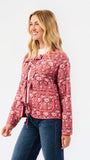 A woman modeling a pink and red floral patterned jacket with tie details and front pockets, paired with blue jeans, against a plain white studio background.