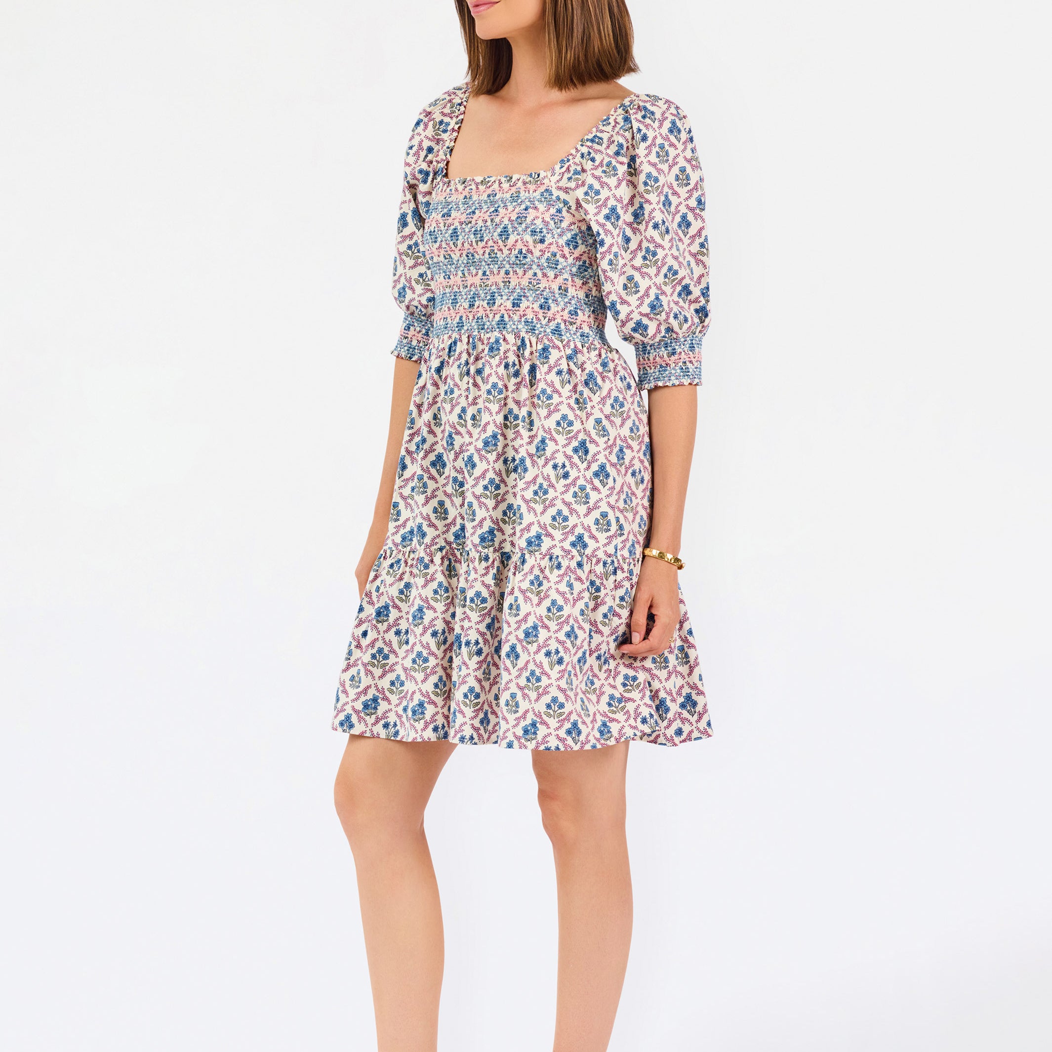 Women with short brown hair wearing a mini dress with puff sleeve lattice printed dress with pink and blue floral wearing gold flats