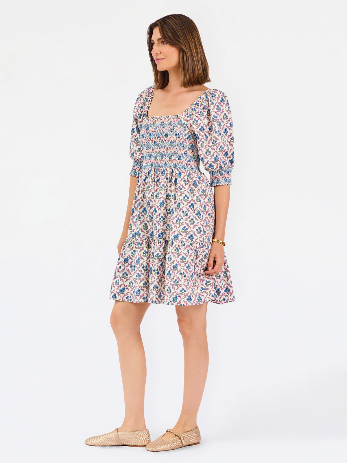 Women with short brown hair wearing a mini dress with puff sleeve lattice printed dress with pink and blue floral wearing gold flats