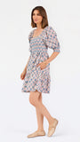 Women with short brown hair wearing a mini dress with puff sleeve lattice printed dress with pink and blue floral wearing gold flats