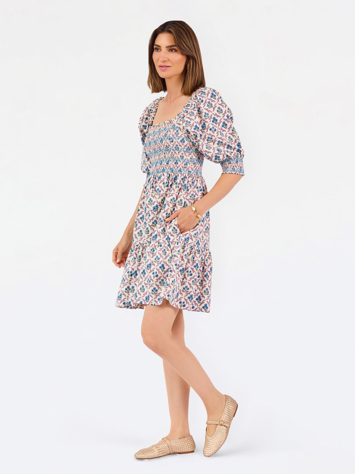 Women with short brown hair wearing a mini dress with puff sleeve lattice printed dress with pink and blue floral wearing gold flats