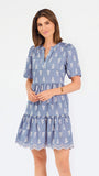 A woman wearing a dusty blue short-sleeve dress with a white floral print, featuring a split neckline and puff sleeves, shown against a plain white background.