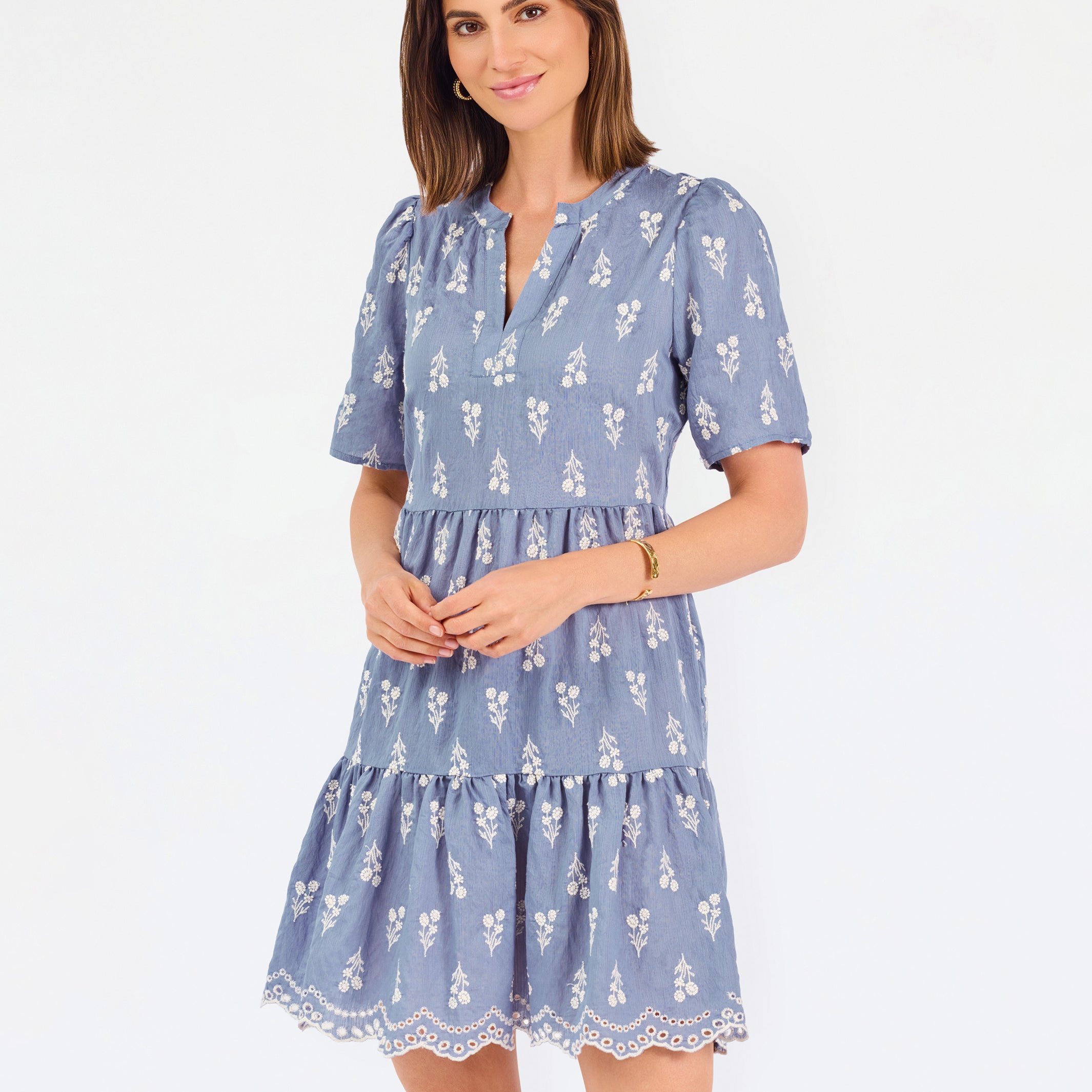 A woman wearing a dusty blue short-sleeve dress with a white floral print, featuring a split neckline and puff sleeves, shown against a plain white background.