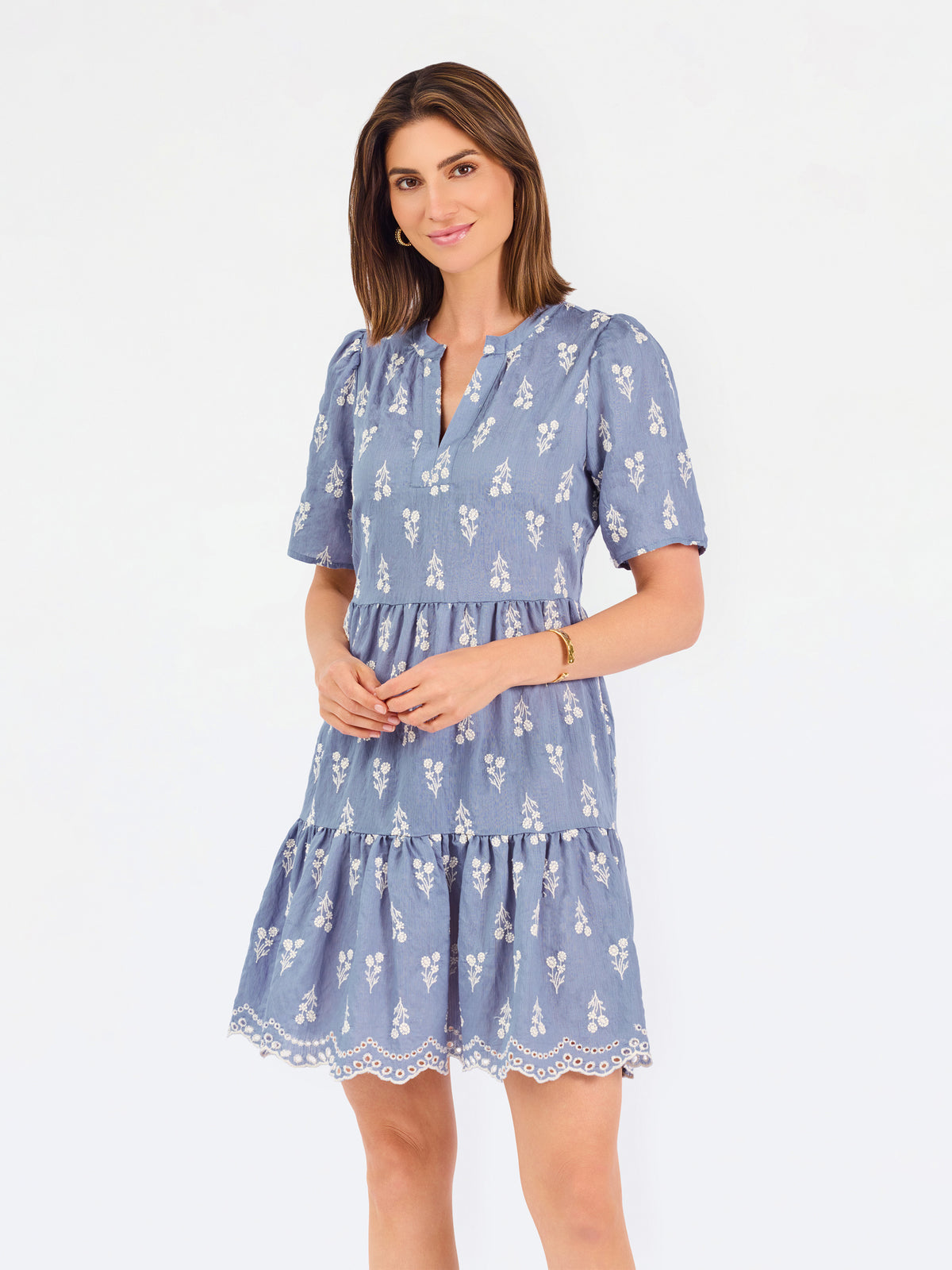 A woman wearing a dusty blue short-sleeve dress with a white floral print, featuring a split neckline and puff sleeves, shown against a plain white background.