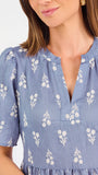 A woman wearing a dusty blue short-sleeve dress with a white floral print, featuring a split neckline and puff sleeves, shown against a plain white background.