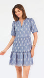 A woman wearing a dusty blue short-sleeve dress with a white floral print, featuring a split neckline and puff sleeves, shown against a plain white background.