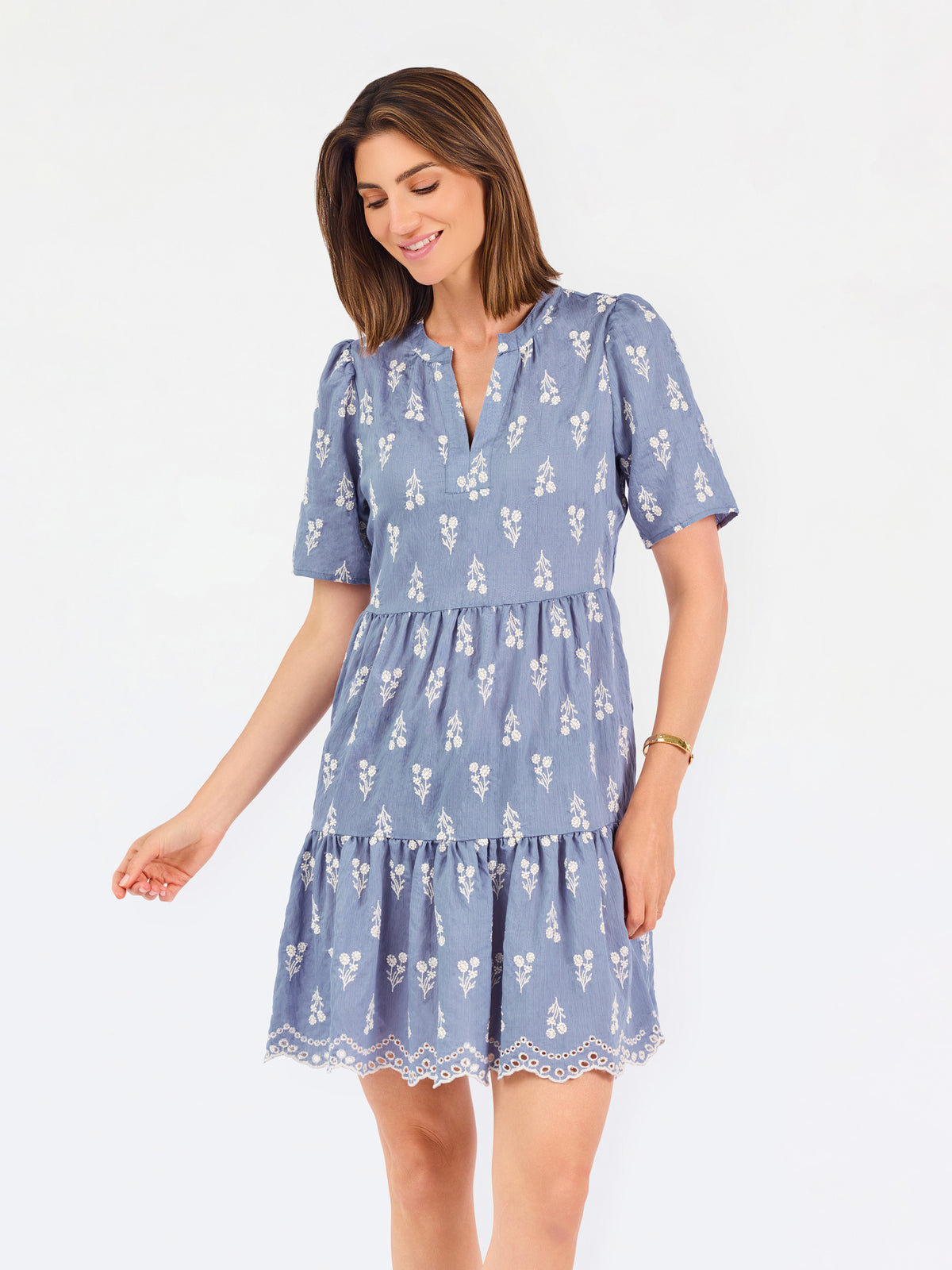 A woman wearing a dusty blue short-sleeve dress with a white floral print, featuring a split neckline and puff sleeves, shown against a plain white background.