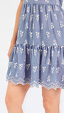 A woman wearing a dusty blue short-sleeve dress with a white floral print, featuring a split neckline and puff sleeves, shown against a plain white background.