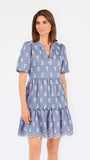 A woman wearing a dusty blue short-sleeve dress with a white floral print, featuring a split neckline and puff sleeves, shown against a plain white background.