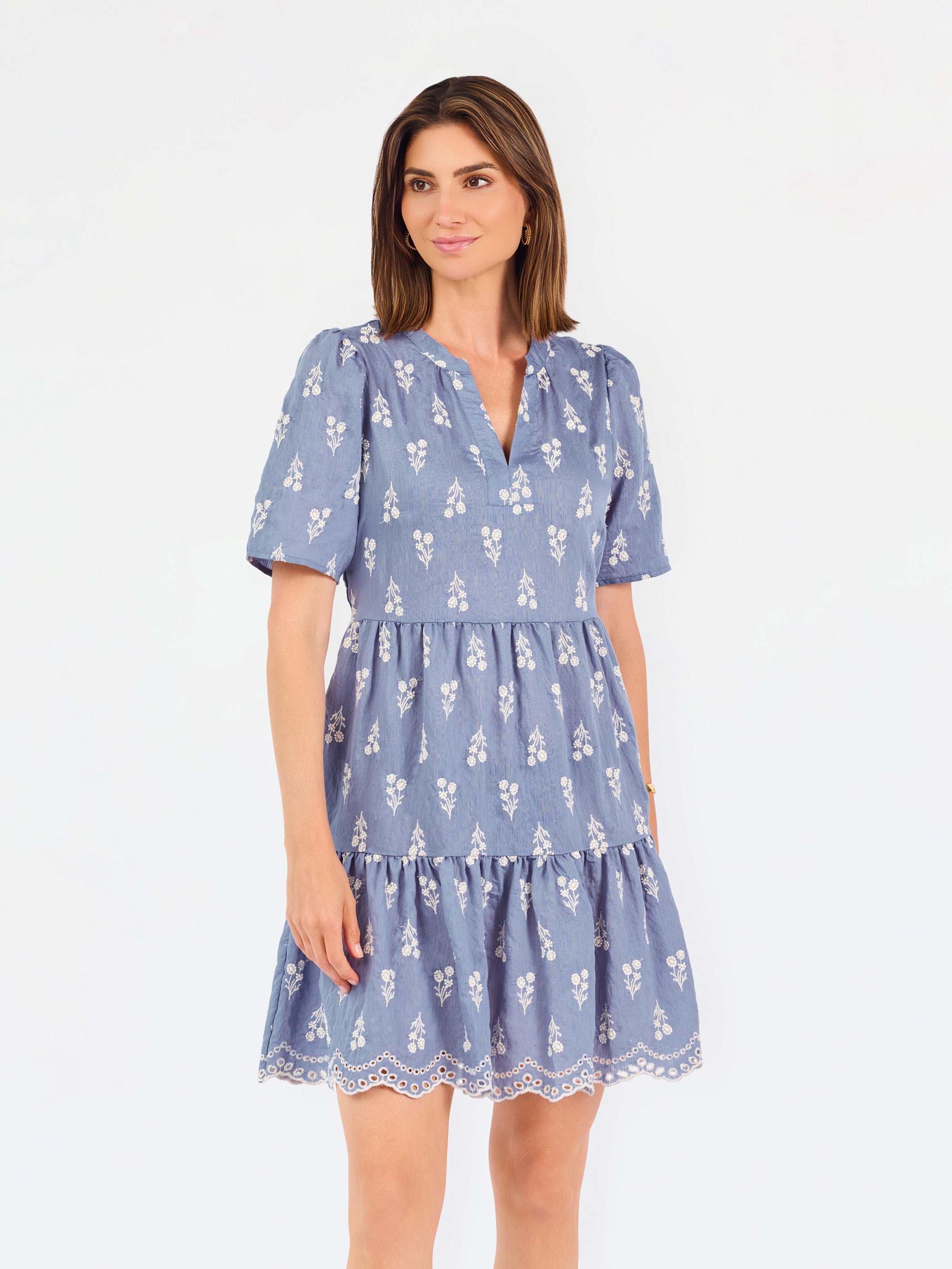 A woman wearing a dusty blue short-sleeve dress with a white floral print, featuring a split neckline and puff sleeves, shown against a plain white background.