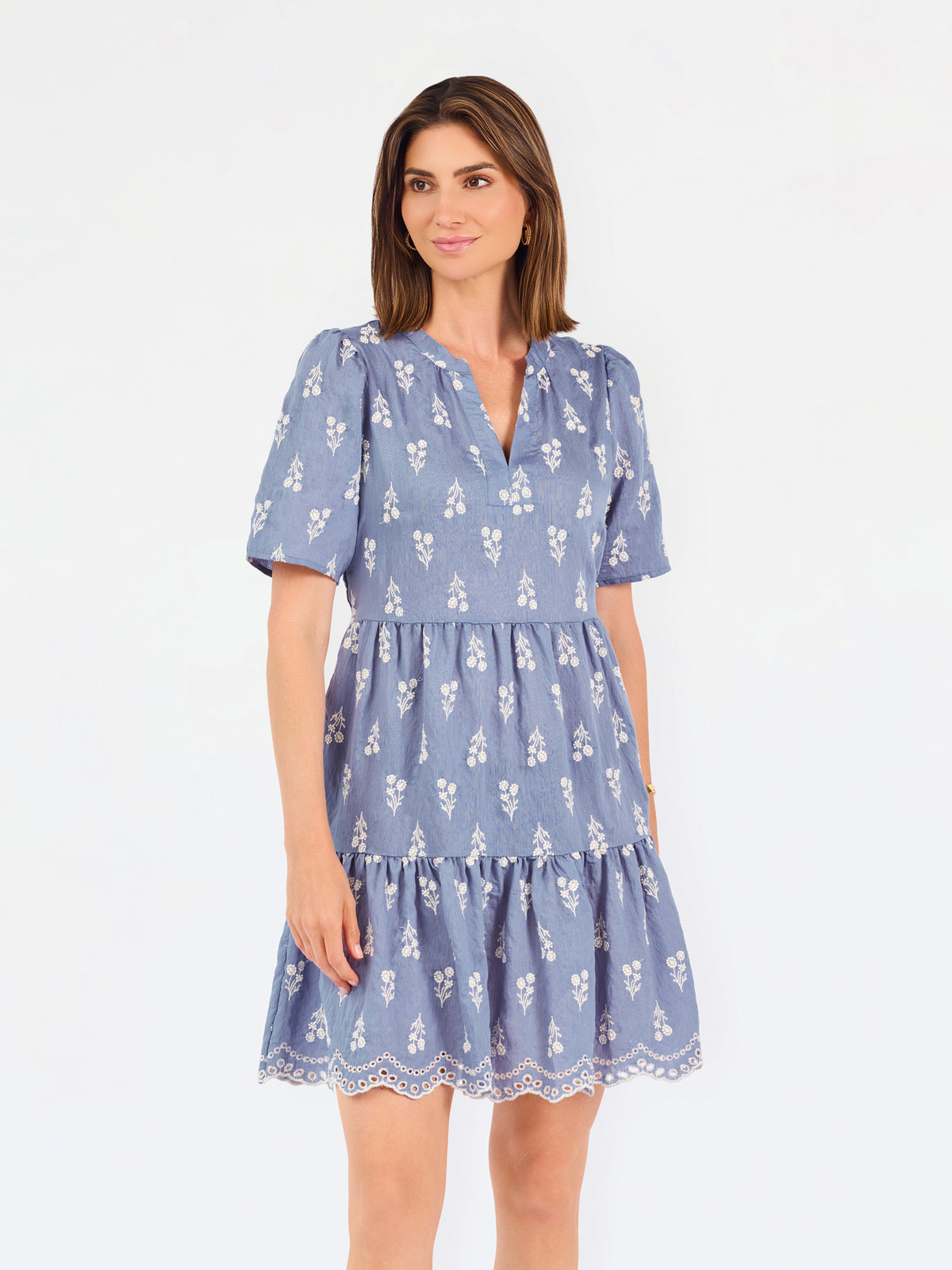 A woman wearing a dusty blue short-sleeve dress with a white floral print, featuring a split neckline and puff sleeves, shown against a plain white background.