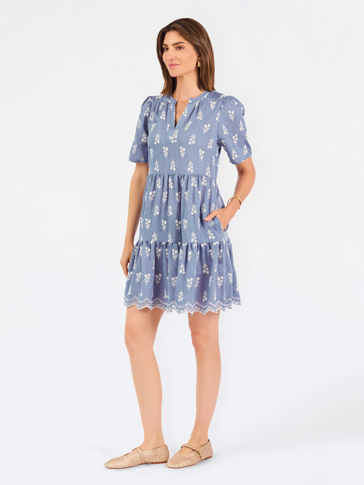 A woman wearing a dusty blue short-sleeve dress with a white floral print, featuring a split neckline and puff sleeves, shown against a plain white background.