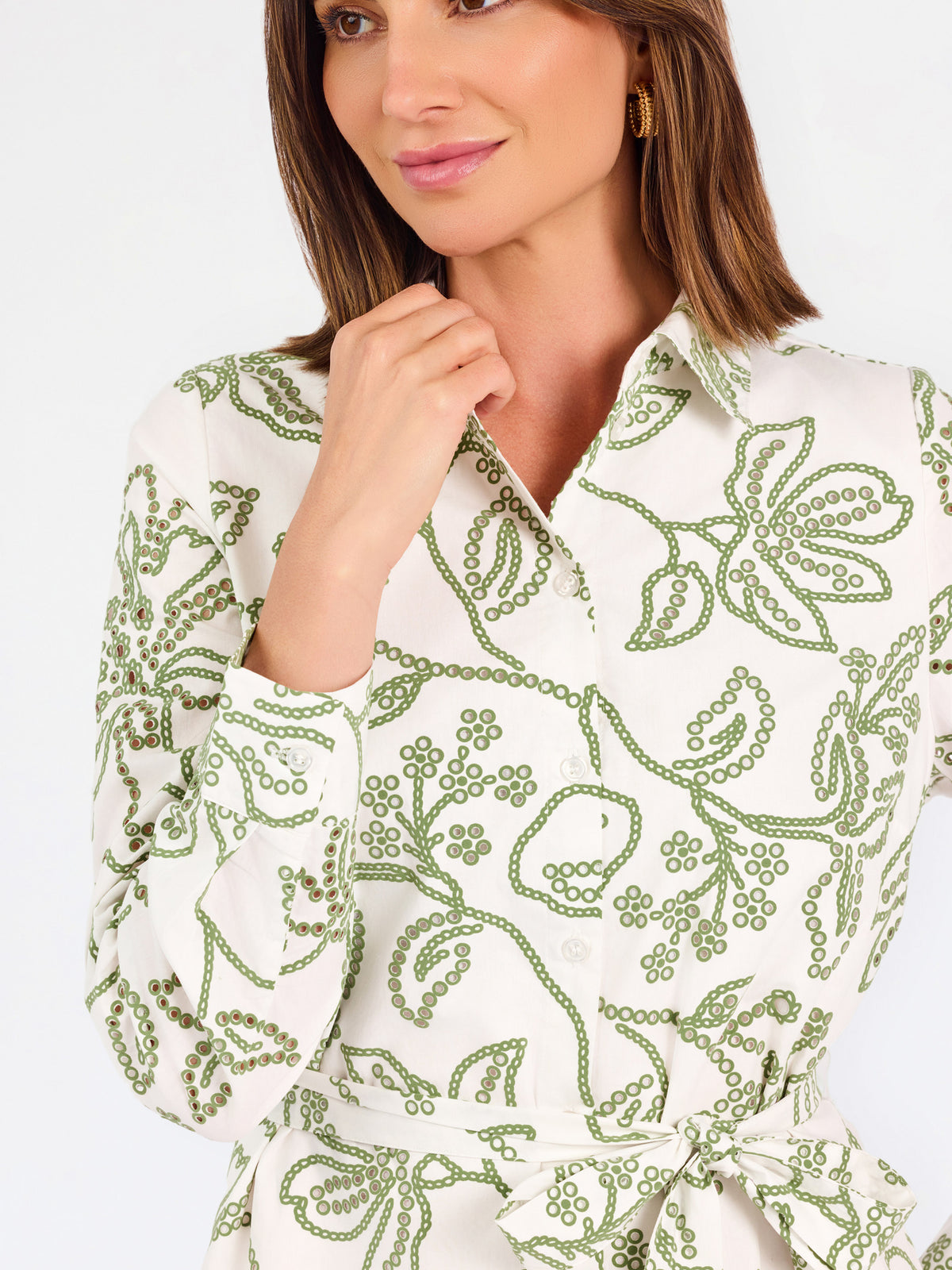 Woman wearing a white long-sleeve button-up dress with green floral embroidery, set against a plain light background.