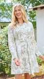 A woman wearing a long-sleeve white shirt dress with a green floral pattern, standing in a garden setting.