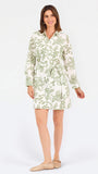 Woman wearing a white long-sleeve button-up dress with green floral embroidery, set against a plain light background.