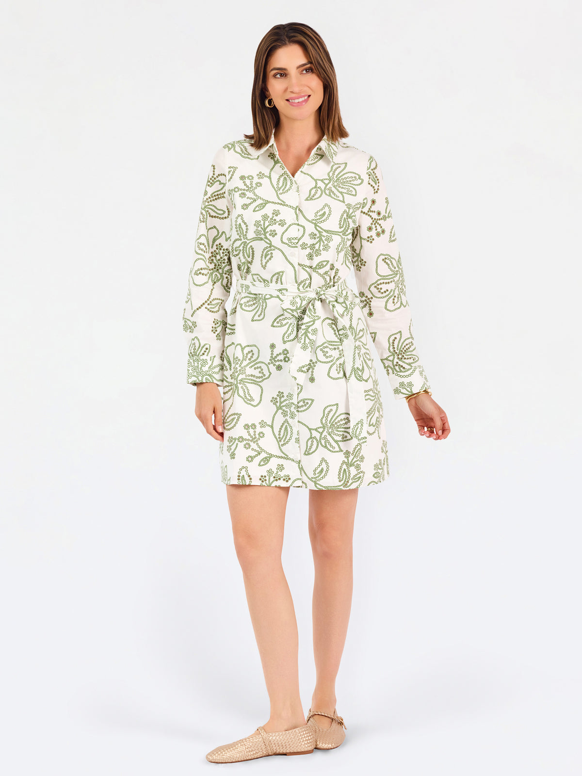 Woman wearing a white long-sleeve button-up dress with green floral embroidery, set against a plain light background.