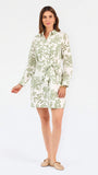Woman wearing a white long-sleeve button-up dress with green floral embroidery, set against a plain light background.