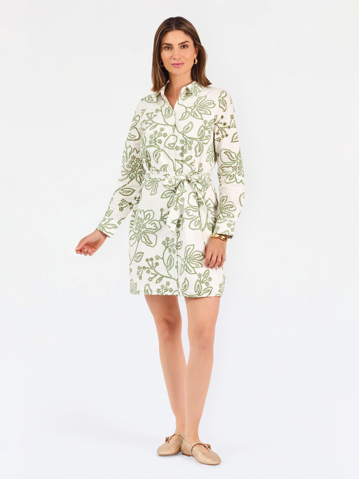 Woman wearing a white long-sleeve button-up dress with green floral embroidery, set against a plain light background.