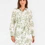 Woman wearing a white long-sleeve button-up dress with green floral embroidery, set against a plain light background.