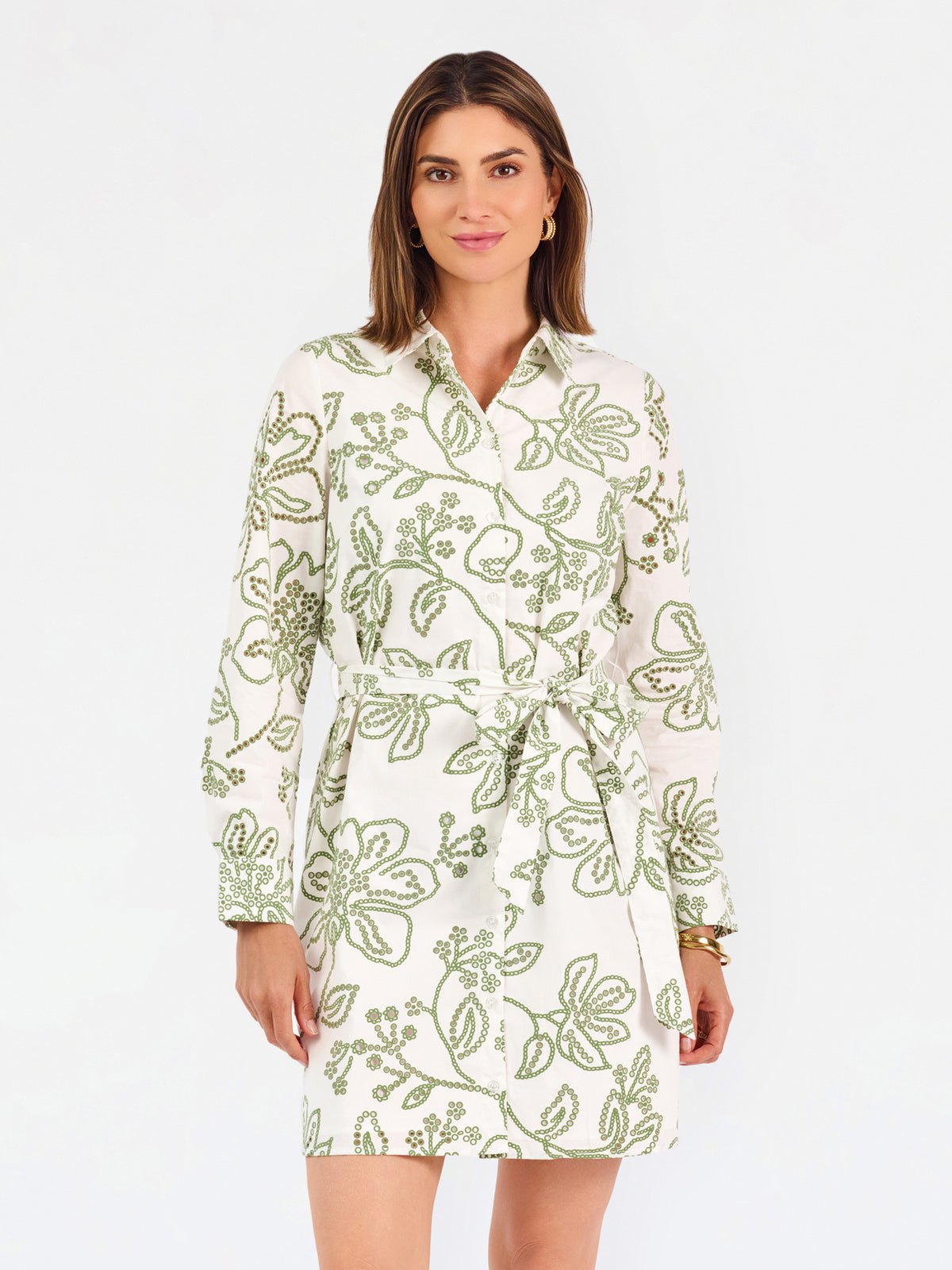 Woman wearing a white long-sleeve button-up dress with green floral embroidery, set against a plain light background.