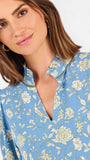 A woman modeling a light blue long-sleeve mini dress with a cream floral print, standing against a plain white studio background.