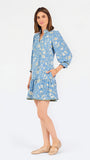 A woman modeling a light blue long-sleeve mini dress with a cream floral print, standing against a plain white studio background.