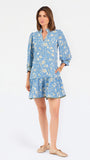 A woman modeling a light blue long-sleeve mini dress with a cream floral print, standing against a plain white studio background.