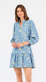 A woman modeling a light blue long-sleeve mini dress with a cream floral print, standing against a plain white studio background.