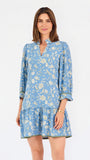 A woman modeling a light blue long-sleeve mini dress with a cream floral print, standing against a plain white studio background.