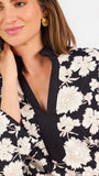 Woman wearing a three quarter sleeve dress with black and tan flowers on a white background. 