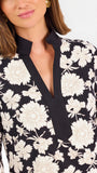 Woman wearing a three quarter sleeve dress with black and tan flowers on a white background. 