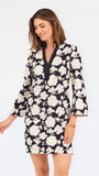 Woman wearing a three quarter sleeve dress with black and tan flowers on a white background. 