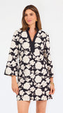 Woman wearing a three quarter sleeve dress with black and tan flowers on a white background. 