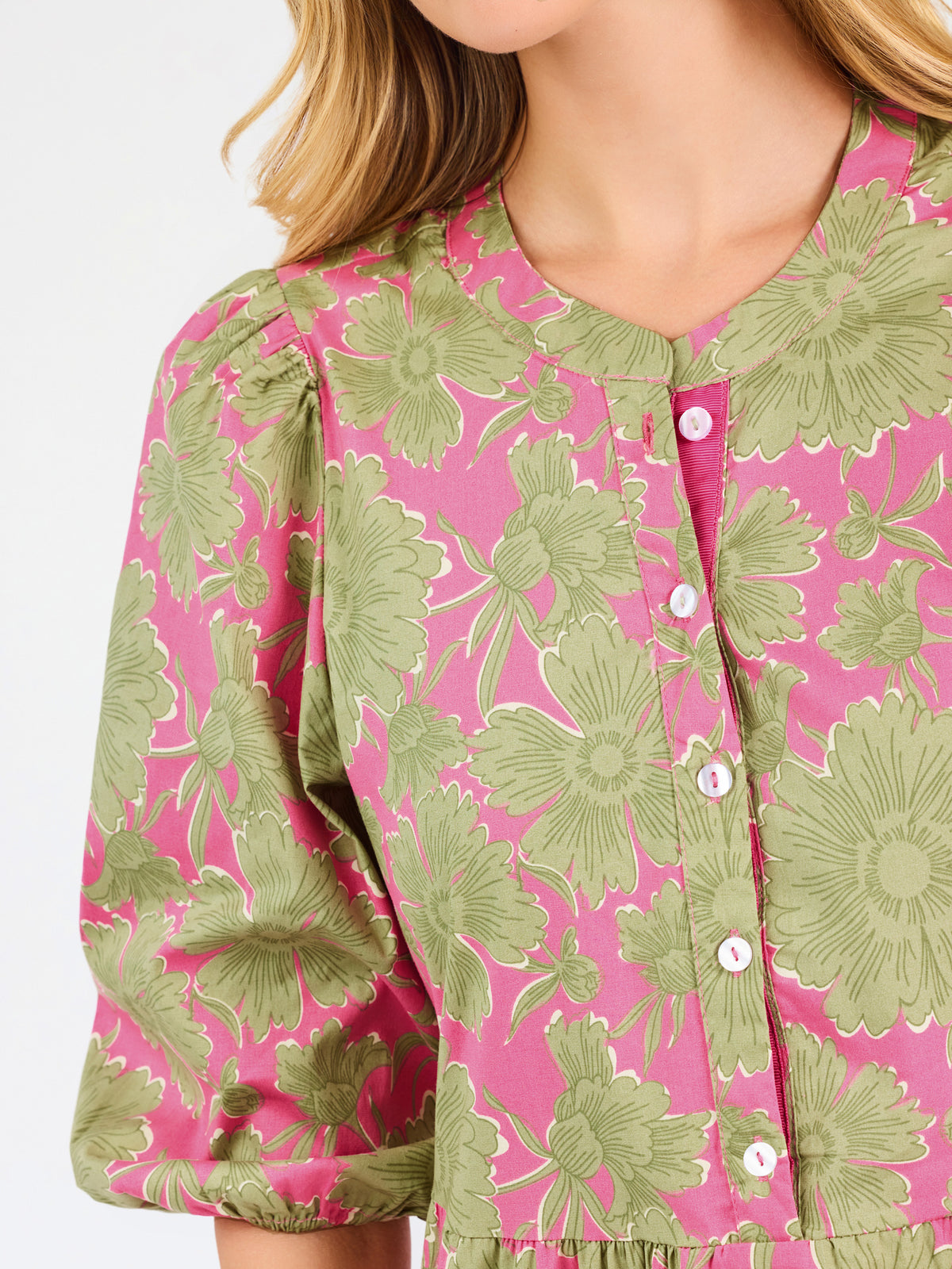 A woman modeling a midi dress with a green and pink floral pattern, short puff sleeves, and a gathered waist, set against a plain white studio background.
