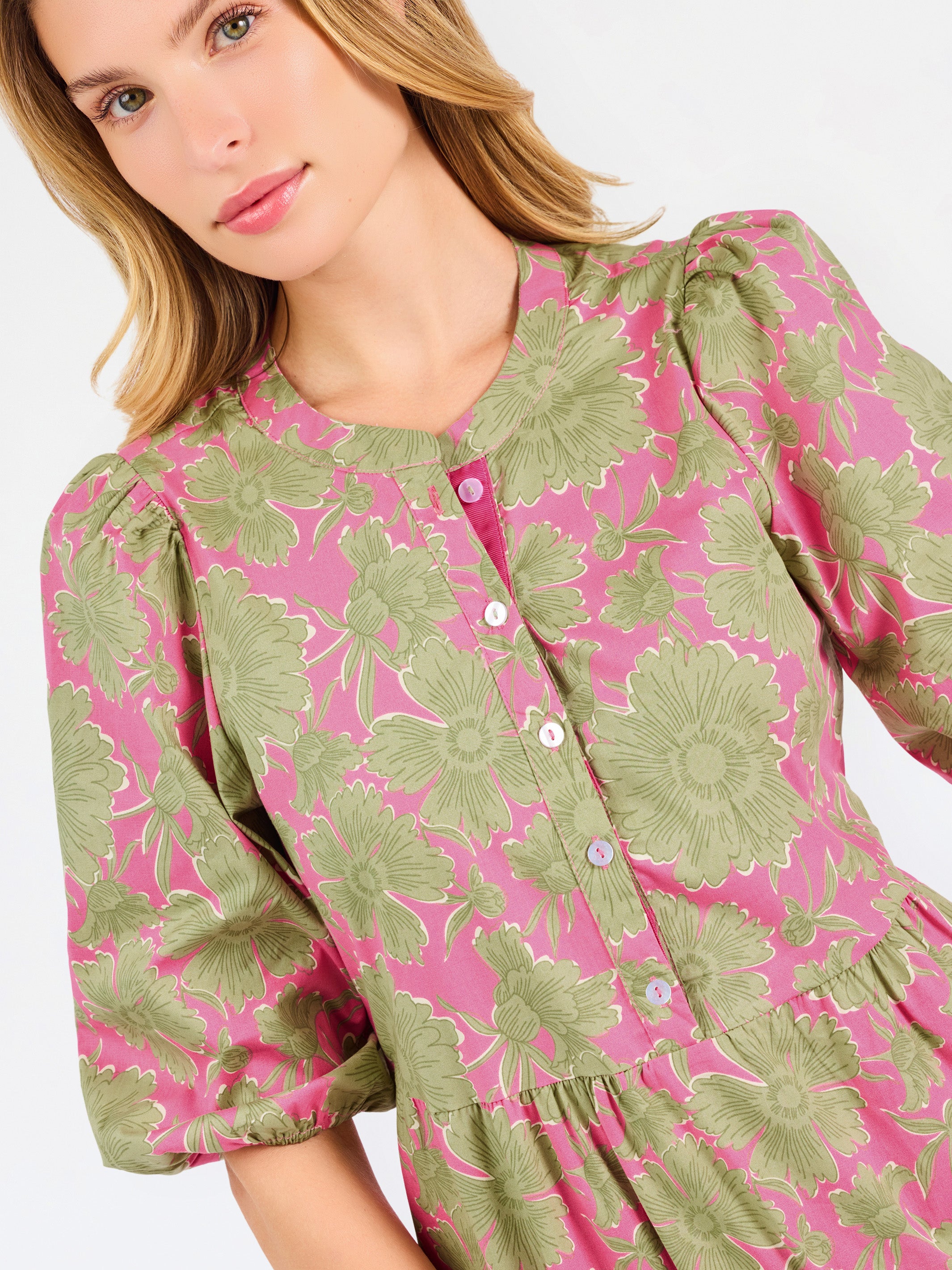 A woman modeling a midi dress with a green and pink floral pattern, short puff sleeves, and a gathered waist, set against a plain white studio background.