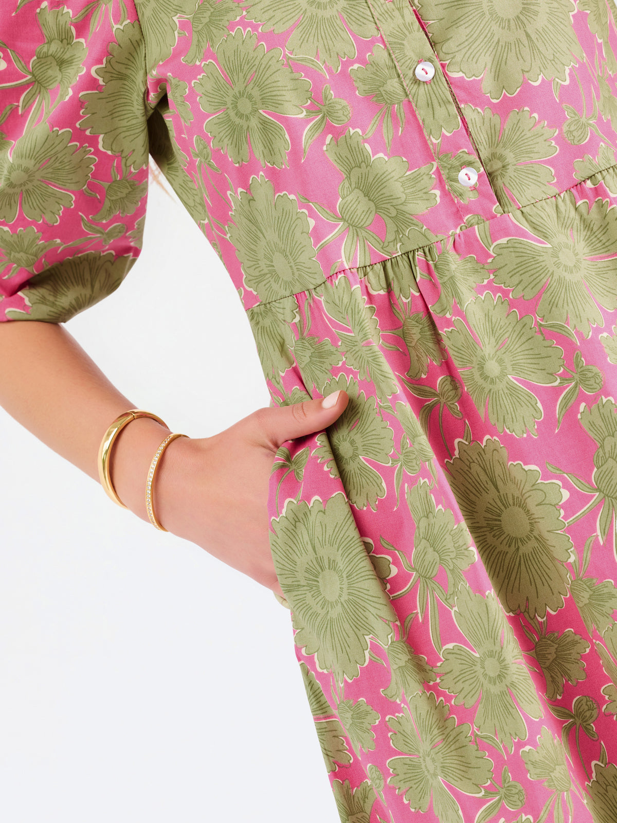 A woman modeling a midi dress with a green and pink floral pattern, short puff sleeves, and a gathered waist, set against a plain white studio background.