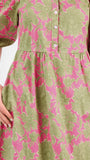 A woman modeling a midi dress with a green and pink floral pattern, short puff sleeves, and a gathered waist, set against a plain white studio background.