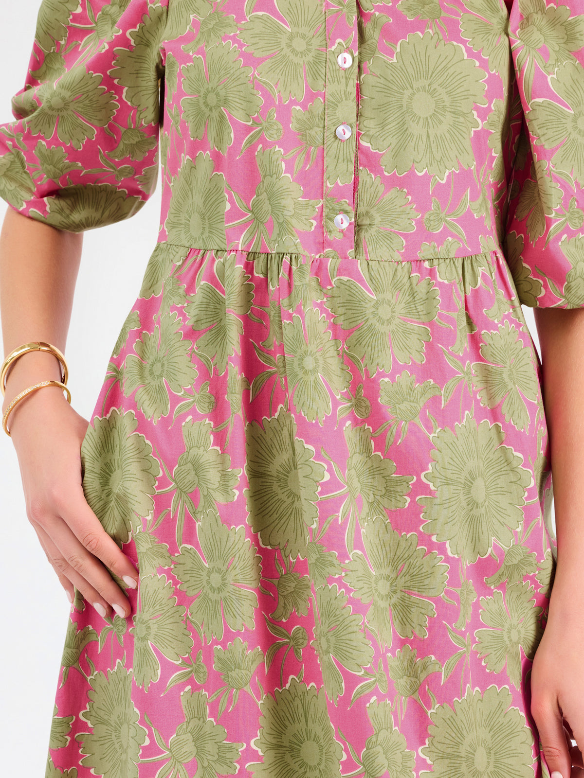 A woman modeling a midi dress with a green and pink floral pattern, short puff sleeves, and a gathered waist, set against a plain white studio background.