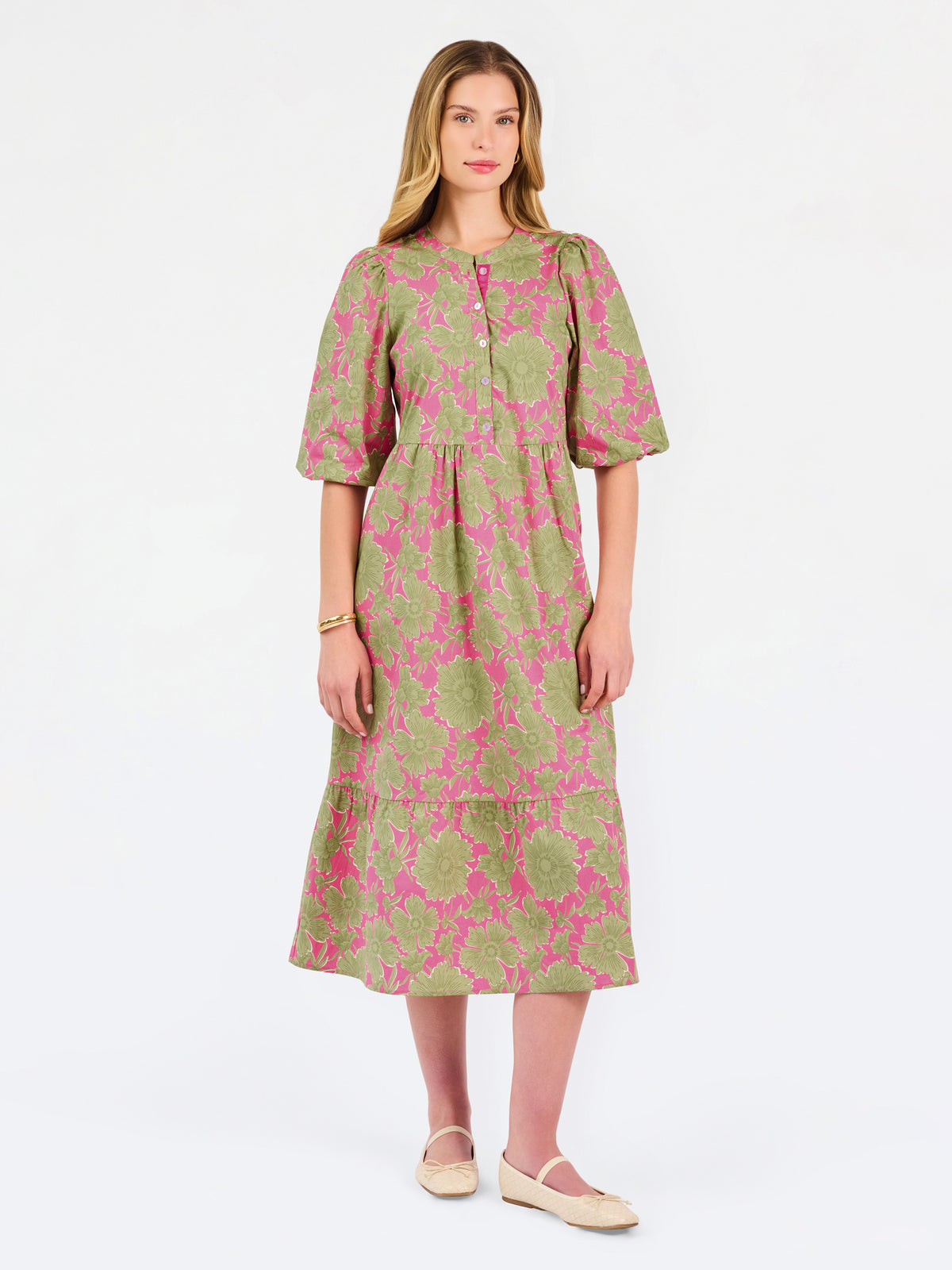 A woman modeling a midi dress with a green and pink floral pattern, short puff sleeves, and a gathered waist, set against a plain white studio background.