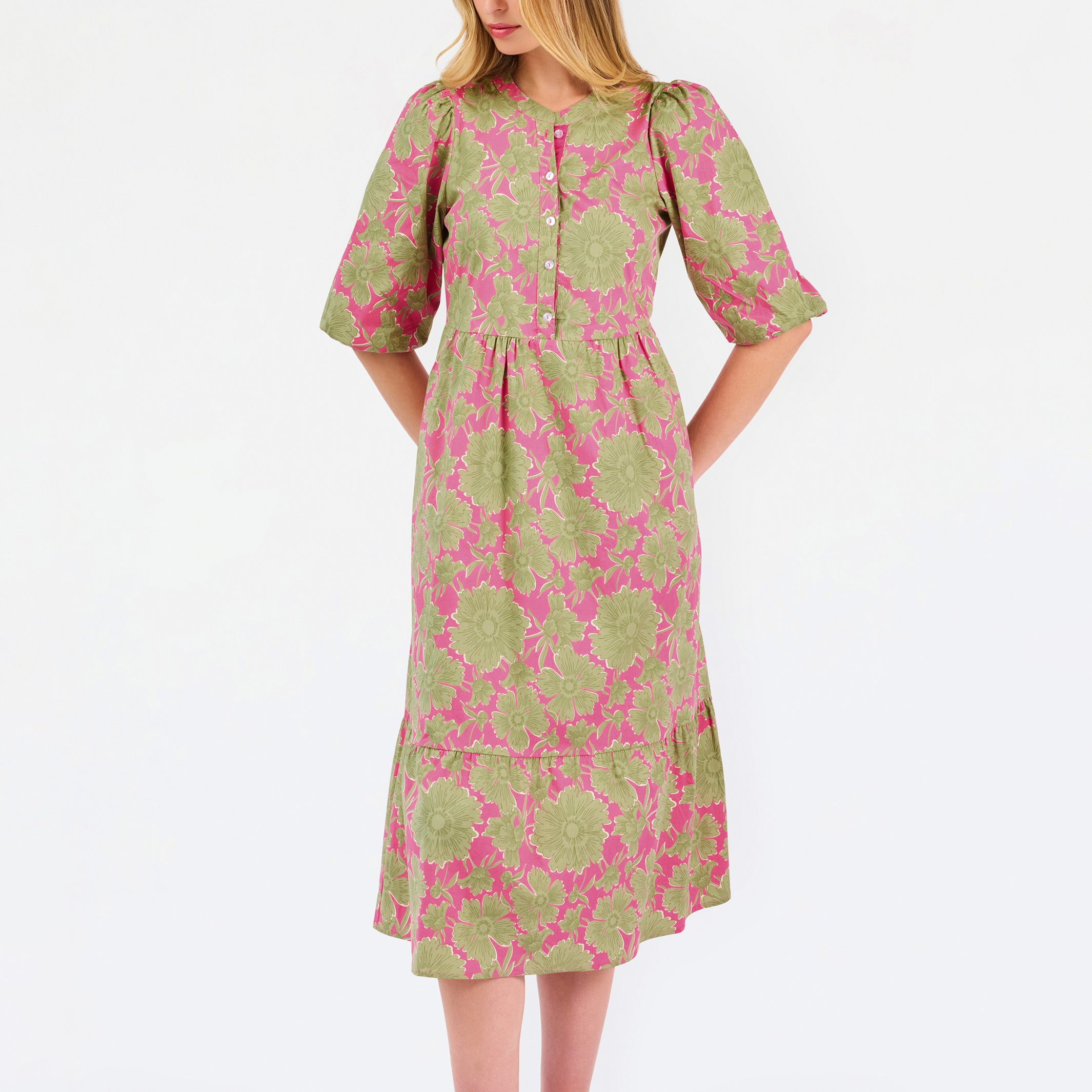 A woman modeling a midi dress with a green and pink floral pattern, short puff sleeves, and a gathered waist, set against a plain white studio background.