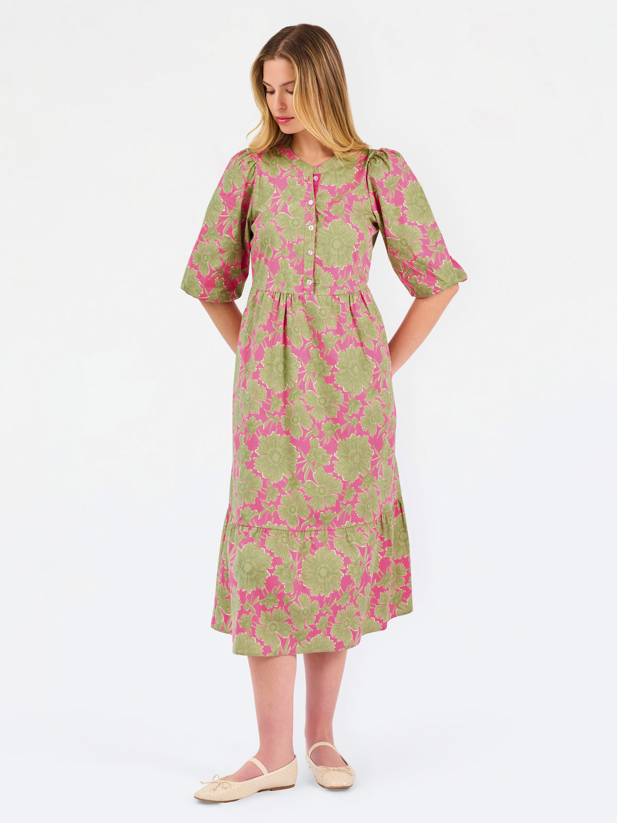 A woman modeling a midi dress with a green and pink floral pattern, short puff sleeves, and a gathered waist, set against a plain white studio background.