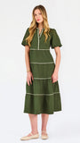 A woman modeling a short-sleeve olive green tiered midi dress with cream-colored piping details, paired with beige flat shoes, against a plain white studio background.