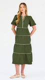 A woman modeling a short-sleeve olive green tiered midi dress with cream-colored piping details, paired with beige flat shoes, against a plain white studio background.