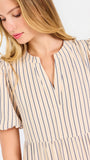 A woman modeling a short-sleeve midi dress with vertical beige and white stripes, featuring a tiered ruffle hem and a split neckline, set against a plain white studio background.