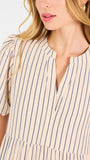 A woman modeling a short-sleeve midi dress with vertical beige and white stripes, featuring a tiered ruffle hem and a split neckline, set against a plain white studio background.