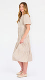 A woman modeling a short-sleeve midi dress with vertical beige and white stripes, featuring a tiered ruffle hem and a split neckline, set against a plain white studio background.