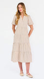 A woman modeling a short-sleeve midi dress with vertical beige and white stripes, featuring a tiered ruffle hem and a split neckline, set against a plain white studio background.