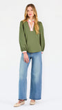 A woman modeling a long-sleeve olive green blouse with a pink and white V-neck trim, paired with blue jeans, against a plain white studio background.