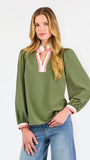 A woman modeling a long-sleeve olive green blouse with a pink and white V-neck trim, paired with blue jeans, against a plain white studio background.